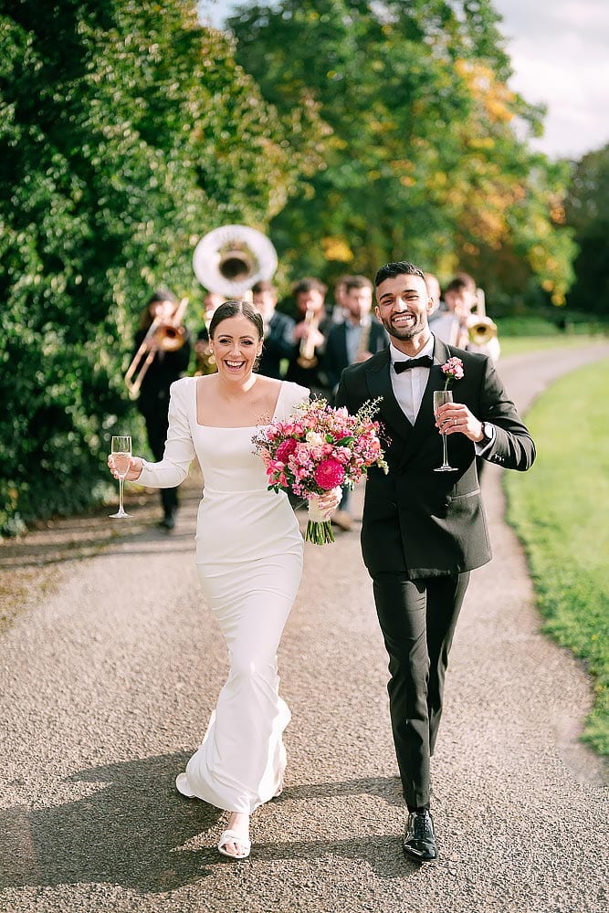 bride and groom walking together in front of brass band